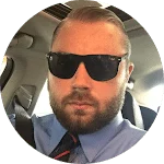 Man with a beard and sunglasses in a car, wearing a blue shirt and tie. Could be related to pressure washing business.