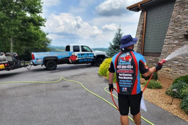 House washing in progress: A worker pressure washes a stone house exterior. A truck with "Blueline" and contact info is visible in the background.