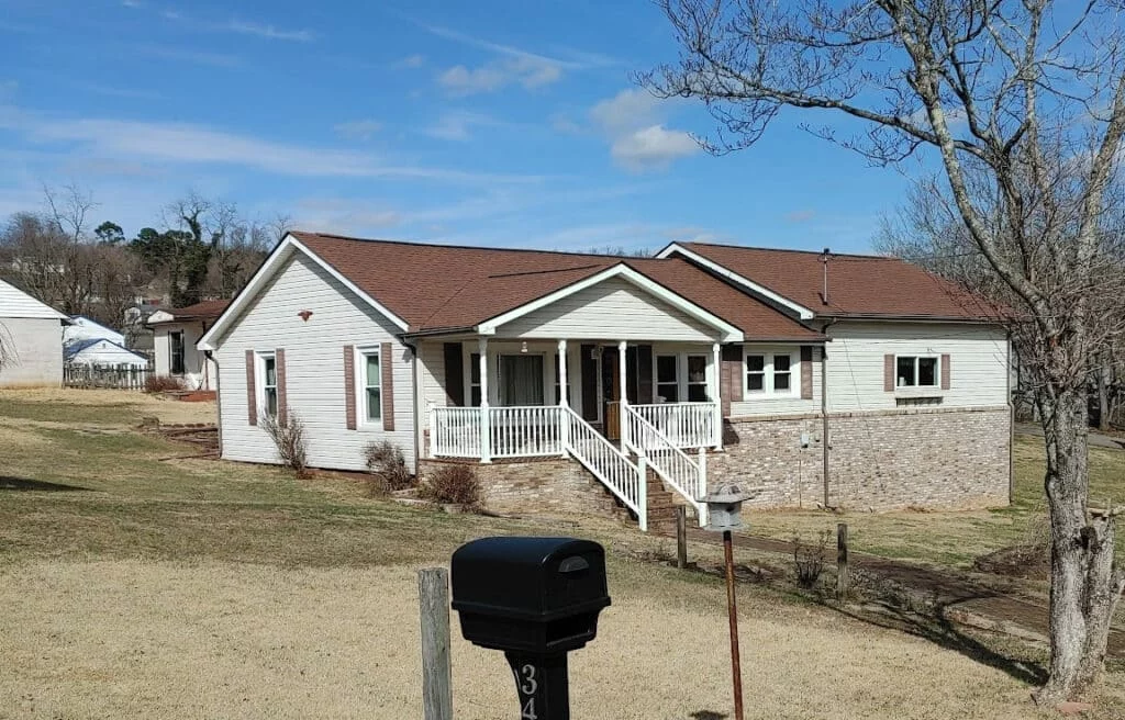 A charming, single-family home with a brown roof, white siding, and a welcoming front porch. Part of the roof is visible, making it relevant for a blog post about roof cleaning tips.