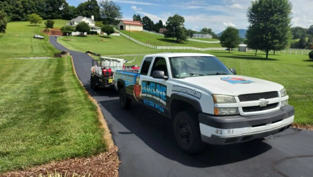 Pressure washing truck and trailer on a freshly cleaned driveway, ready for spring cleaning. The truck has company branding on the side and a house is visible in the background.