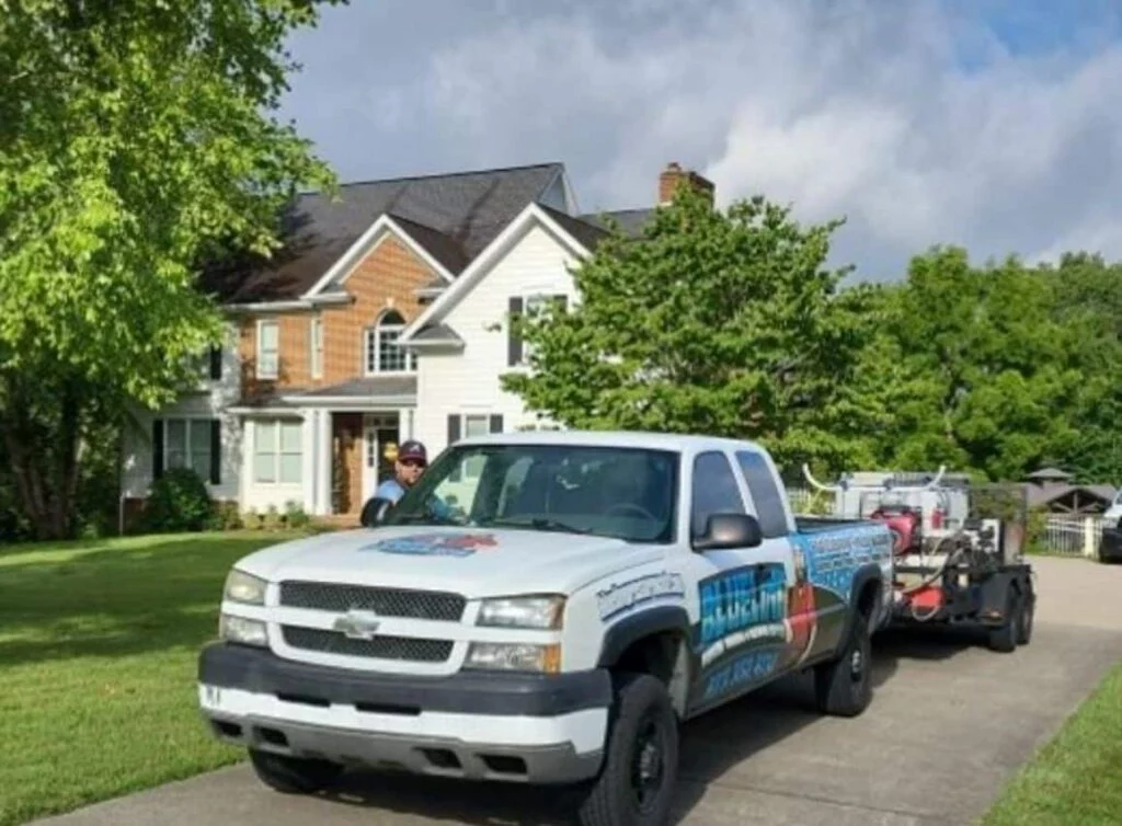 A white pressure washing truck with equipment parked on a driveway in front of a large brick and white house. Getting ready for pressure washing before Thanksgiving to clean up the exterior.