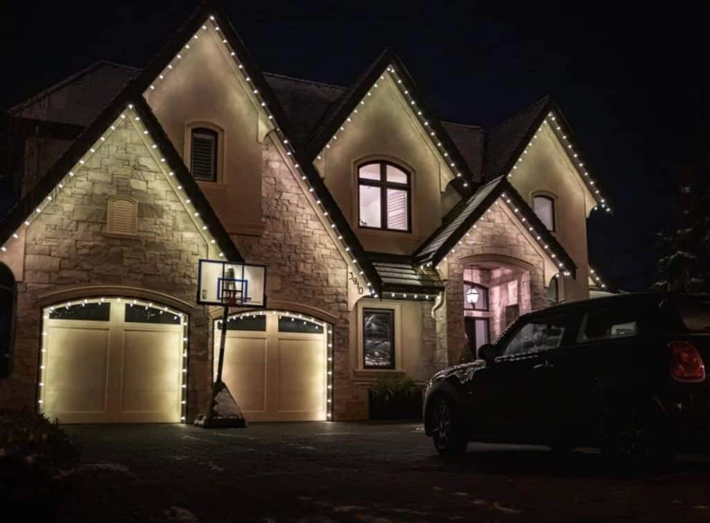 Tri Cities home with warm white Christmas lights outlining the roofline and garage doors. A dark car sits in the driveway, and a basketball hoop stands near the garage.