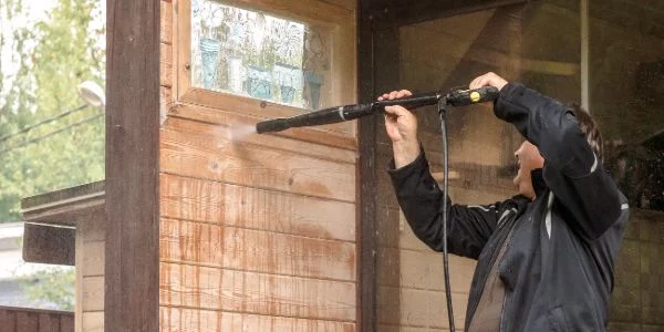 A man power washing the exterior siding of a house. The water stream is visible as he cleans, showcasing the process of power washing or pressure washing.