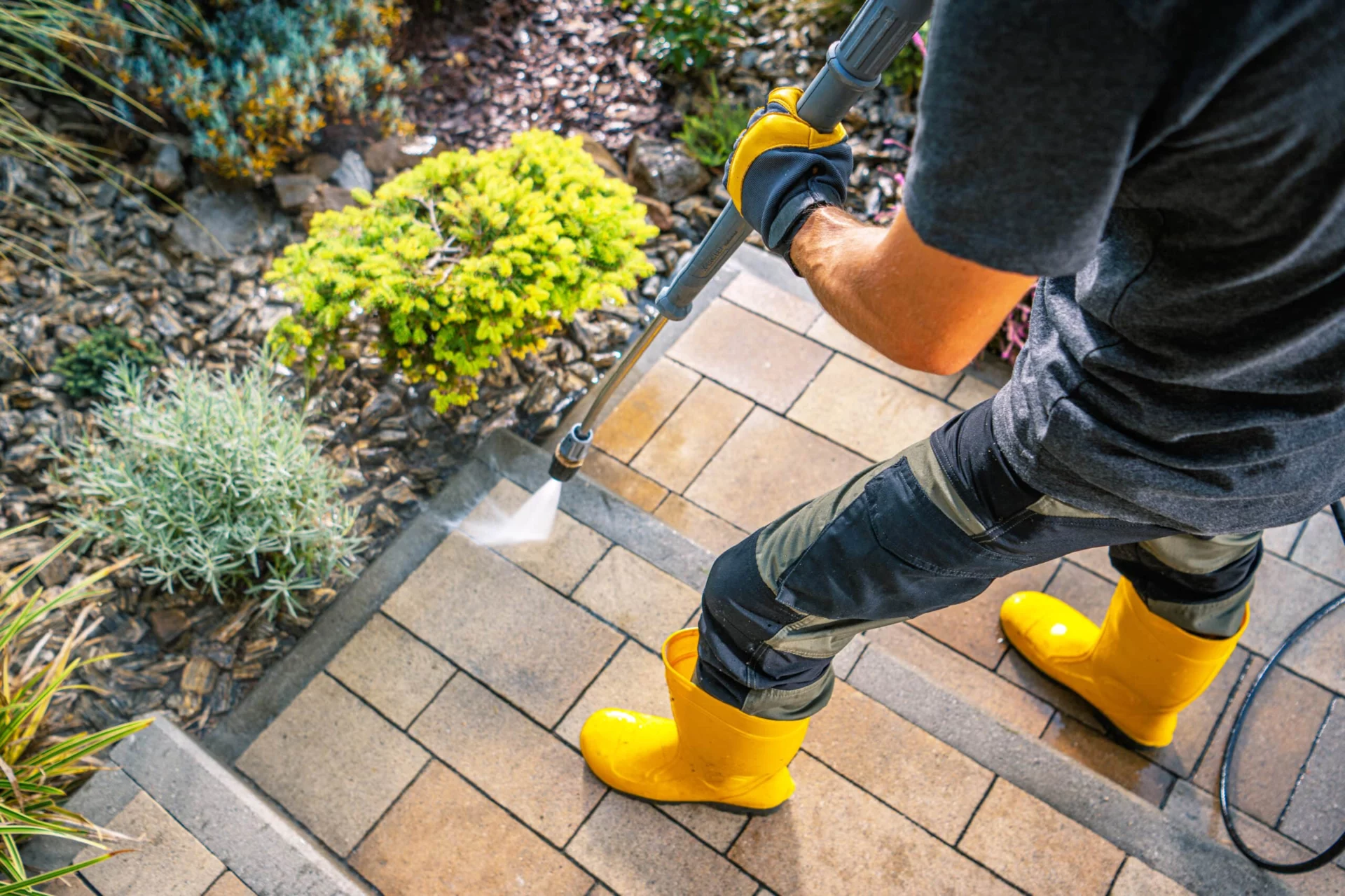 A person power washing a brick stairway with yellow boots, showcasing home maintenance. The scene emphasizes the process of how often a house should be power washed.