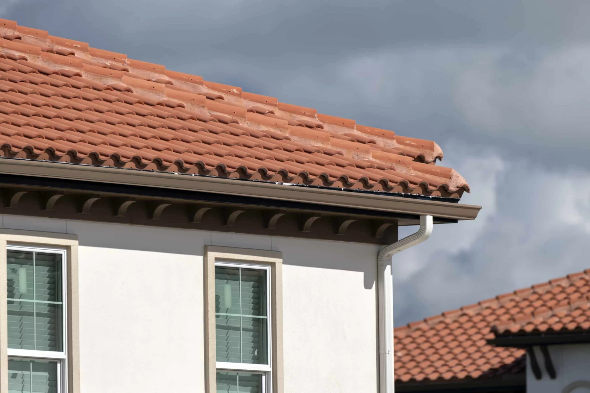 Close-up of a house with a terracotta tile roof, brown gutters, and white stucco walls, showcasing a soft wash-friendly exterior cleaning scenario.