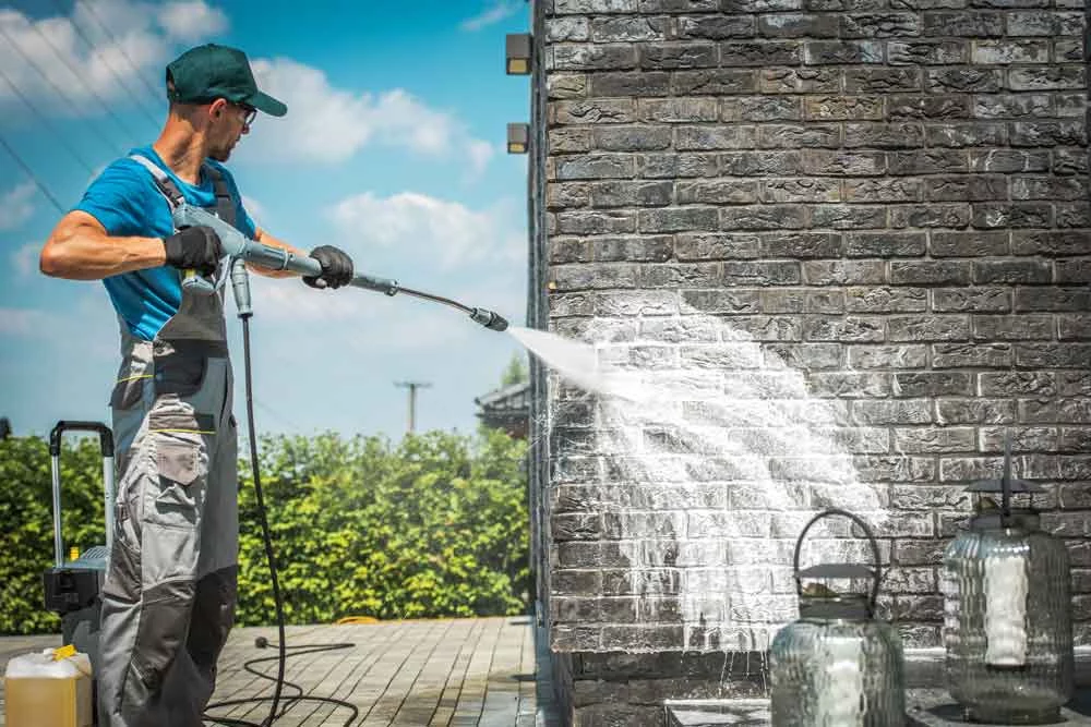 A man power washing a brick wall. Using power washing techniques, he cleans the exterior of a building with a high-pressure stream of water, removing dirt and grime.