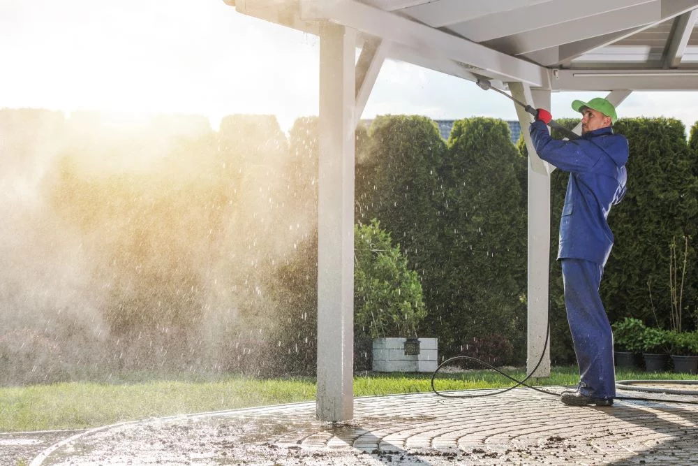 A worker in blue overalls uses a power wash to clean a white patio cover. The powerful spray removes grime, highlighting the importance of gentle pressure when power washing siding.