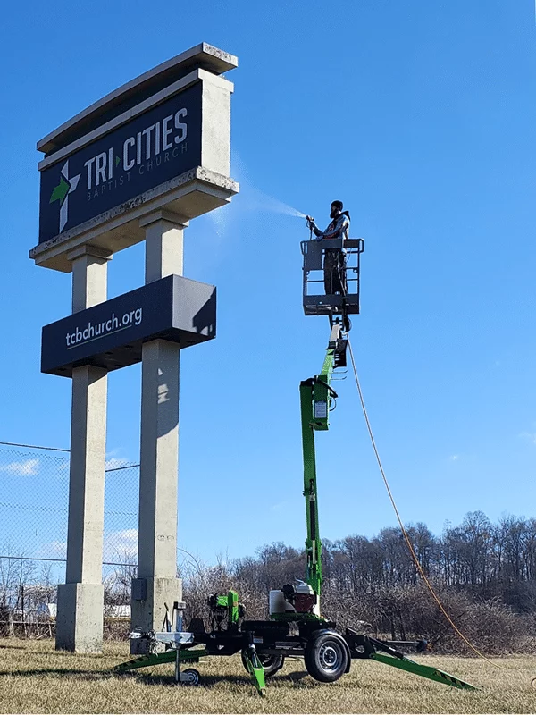 A worker power washing the Tri-Cities Baptist Church sign using a boom lift. The sign also reads tcbchurch.org. The image relates to commercial power washing regulations.