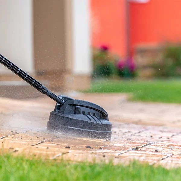 Power washing a brick patio with a surface cleaner attachment. Water sprays as the tool removes dirt and grime, demonstrating how long power washing should take.
