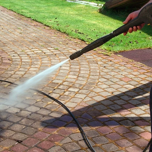 Power washing a brick patio. A person uses a pressure washer to clean a red and gray brick walkway, removing dirt and grime with a powerful spray of water.